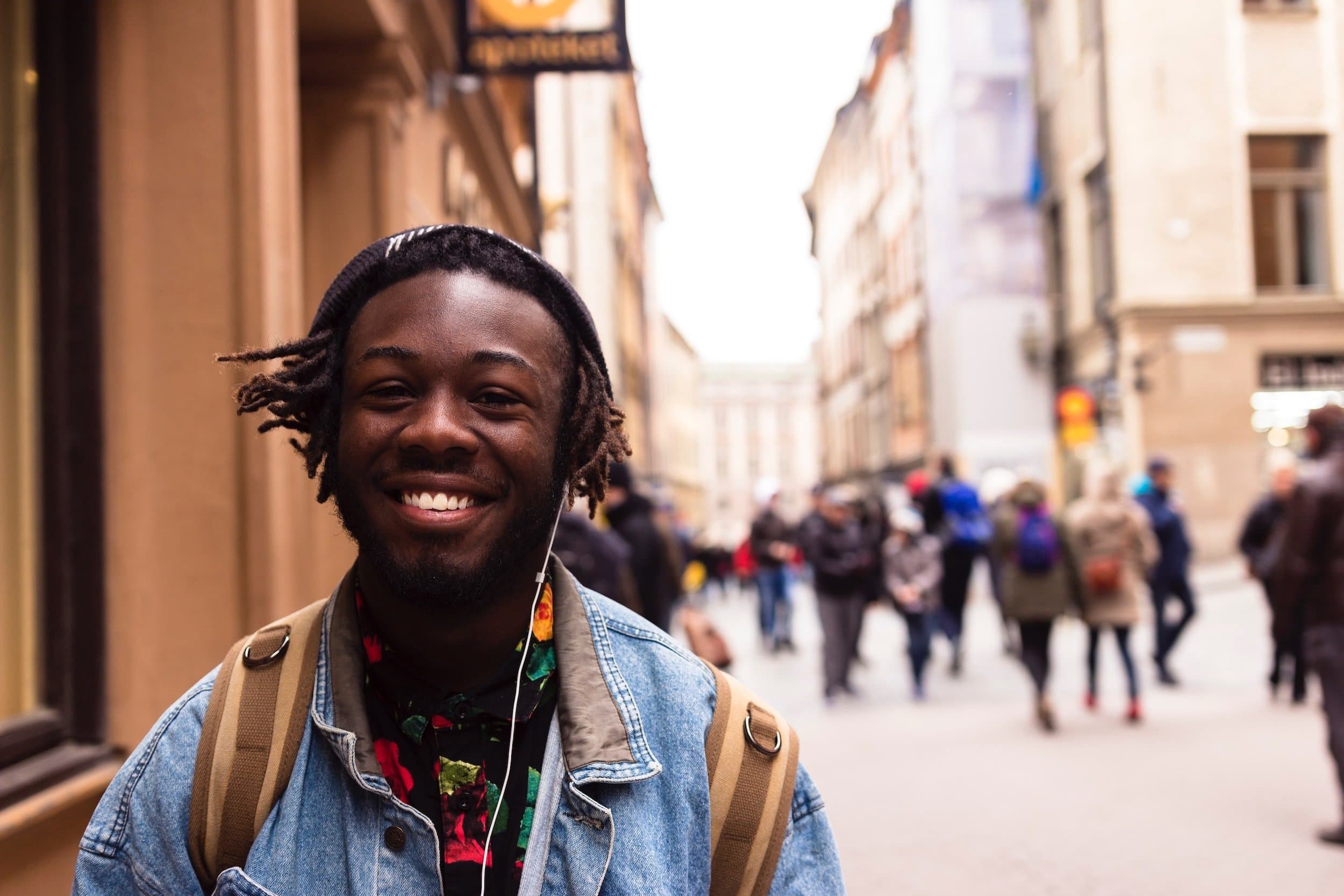 Young African American wearing a beanie with headphones and a backpack walking down a street